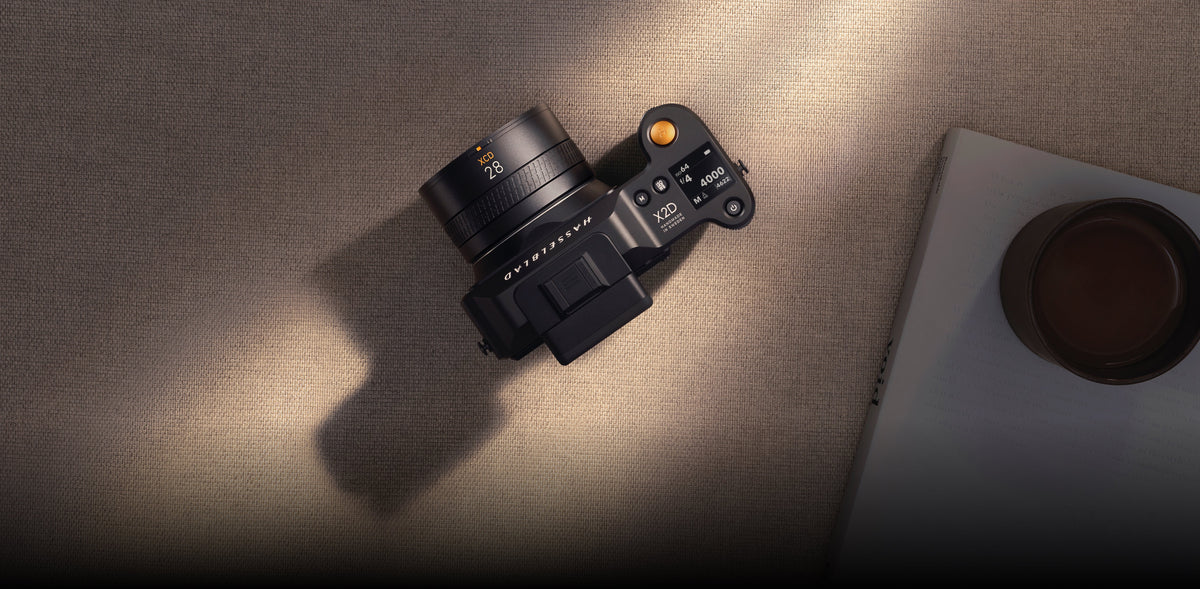 Hasselblad X2D Kamera mit 28-mm-Objektiv neben Buch und Kaffeetasse im warmen Sonnenlicht