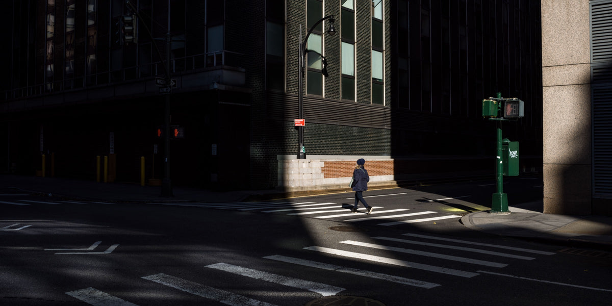 Dunkle Straßenszene in der Stadt mit einem Fußgänger im Sonnenlicht zwischen hohen Gebäuden.