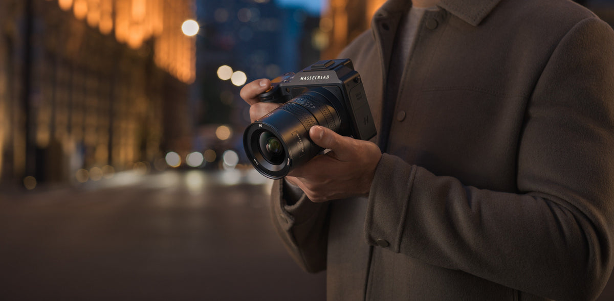Person hält eine Hasselblad-Kamera mit Weitwinkelobjektiv bei Nacht in einer beleuchteten Stadt