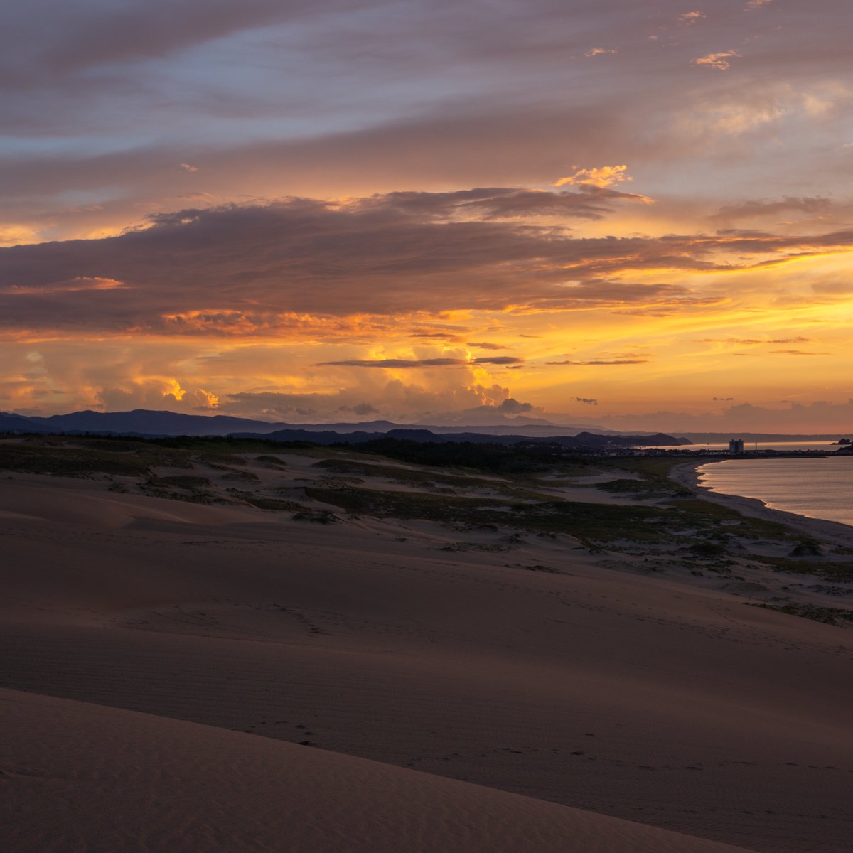 Sonnenaufgang über einer Küstenlandschaft mit Sanddünen und orangefarbenen Wolken